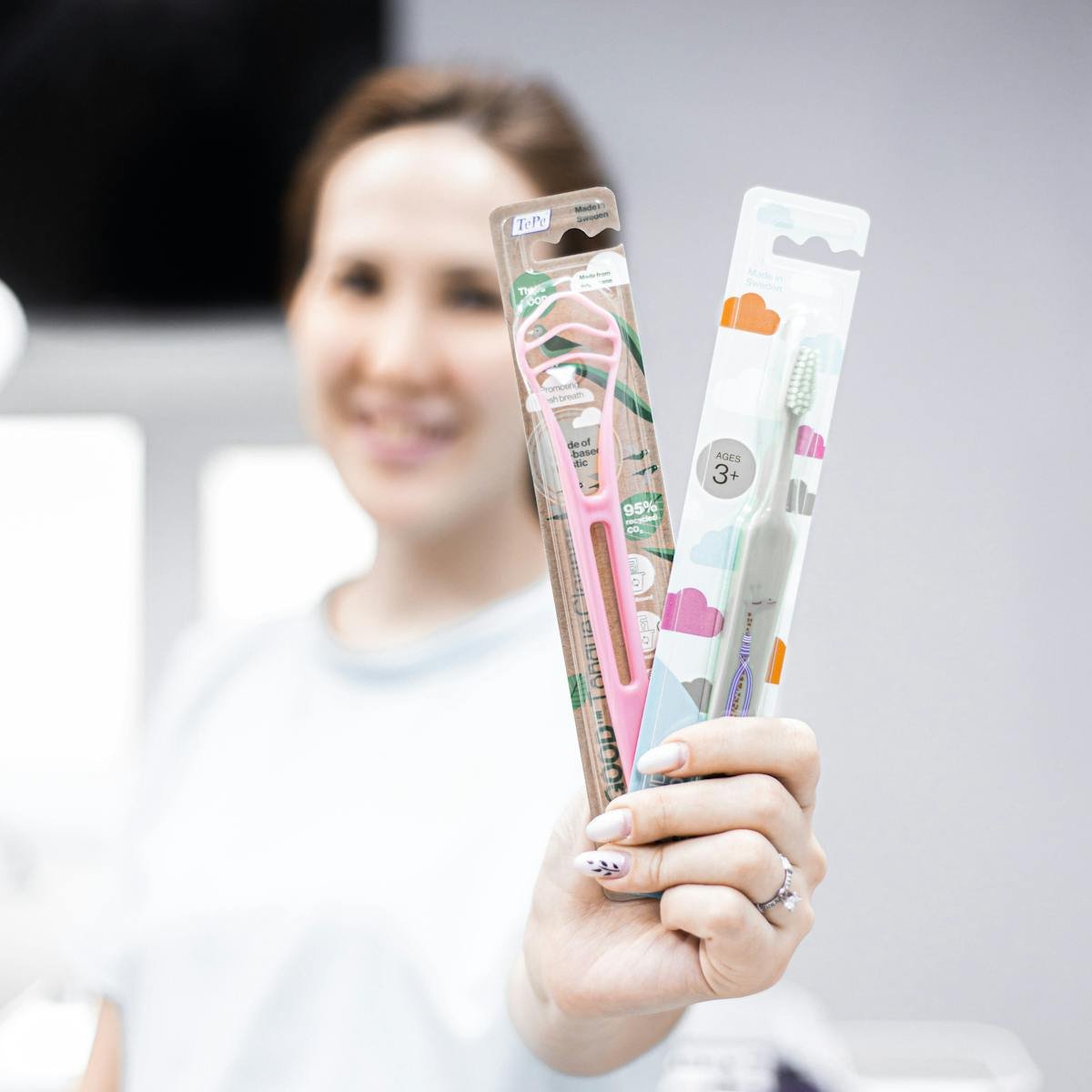 Close-up of a woman holding packaged dental hygiene products, smiling in the background.