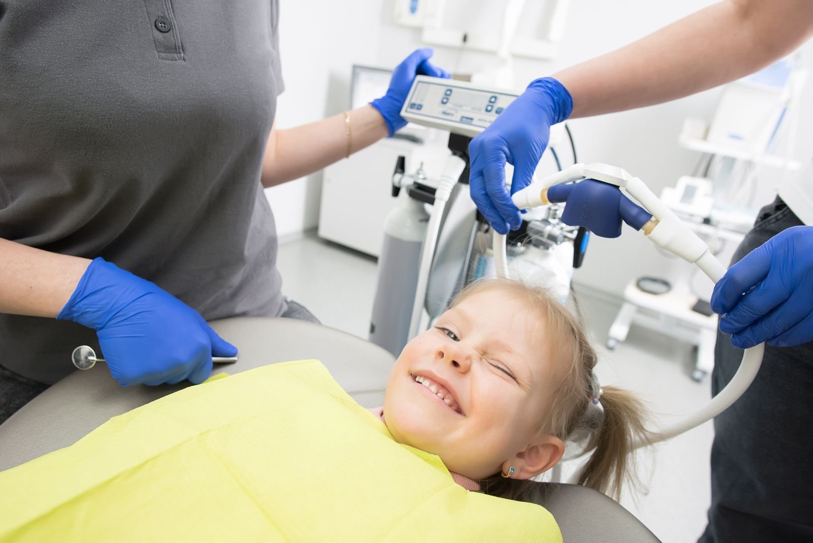 AI for Dental Anxiety in Kids: Calm or a Slower Pulse? A cheerful child winks while sitting in a dental chair, surrounded by dental professionals.